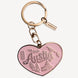 A pink heart-shaped keychain charm with 'Austin' and local landmarks engraved, attached to a rose gold split ring and keychain hardware on a light gray background.