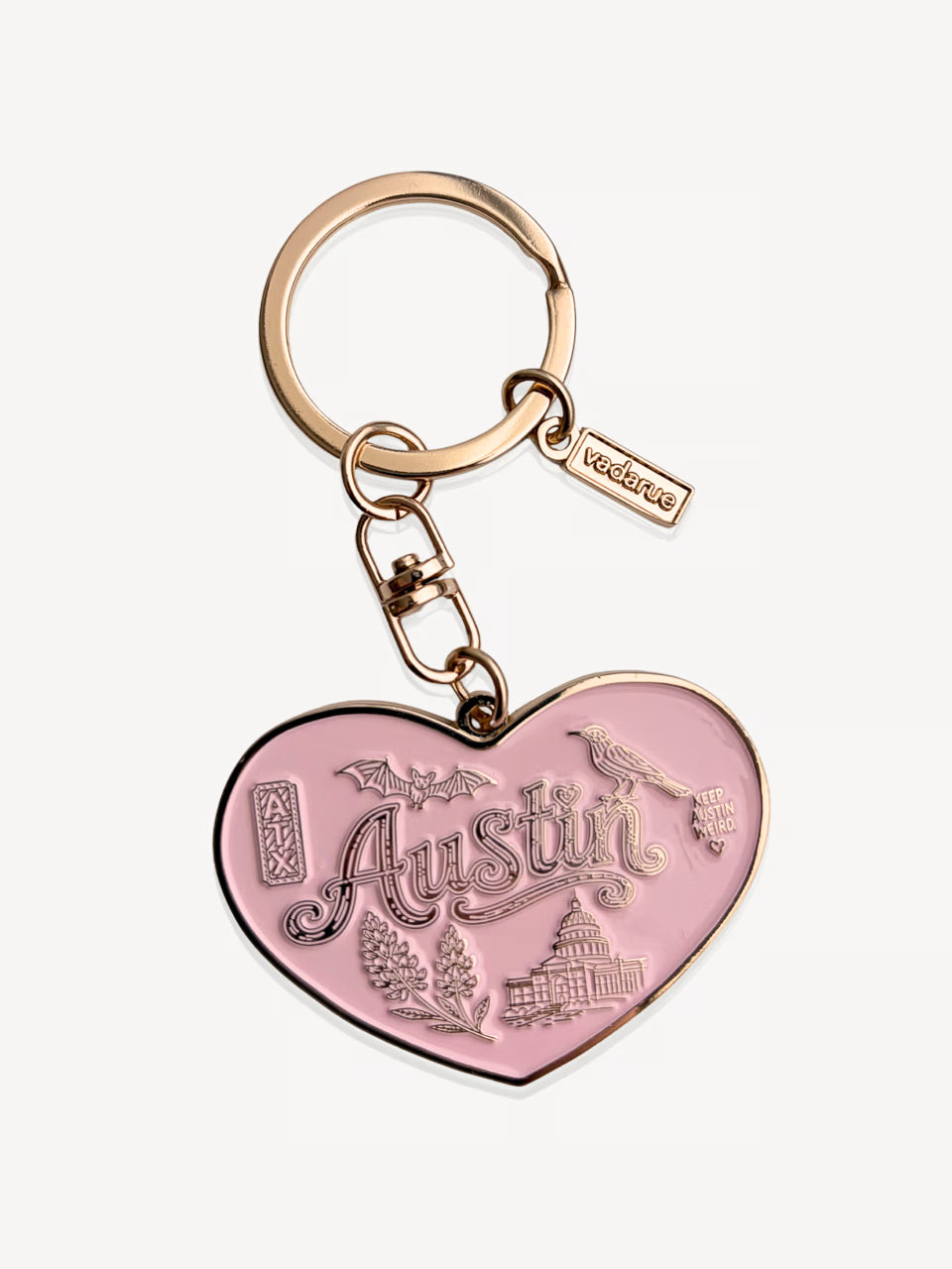A pink heart-shaped keychain charm with 'Austin' and local landmarks engraved, attached to a rose gold split ring and keychain hardware on a light gray background.