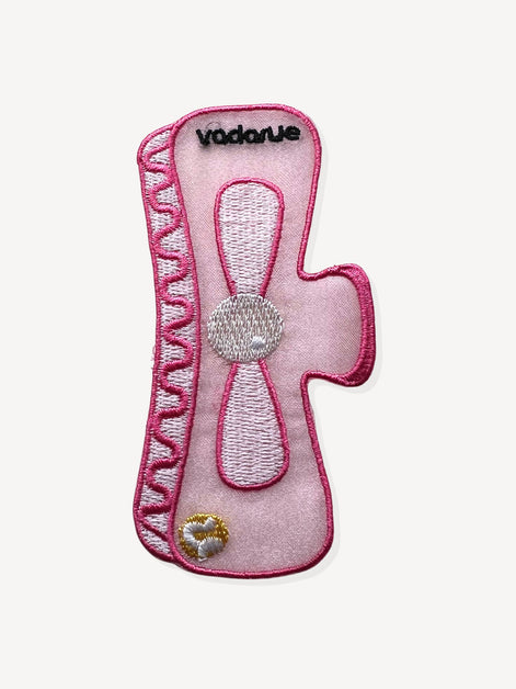 An embroidered pink bookmark patch with the brand name 'vadarue' stitched in black at the top