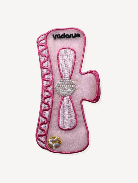 An embroidered pink bookmark patch with the brand name 'vadarue' stitched in black at the top