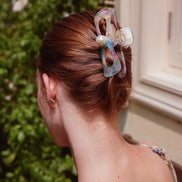 A woman shown from the back wearing a translucent iridescent cellulose acetate hair claw clip with a pearl accent, holding her auburn hair in a low bun.