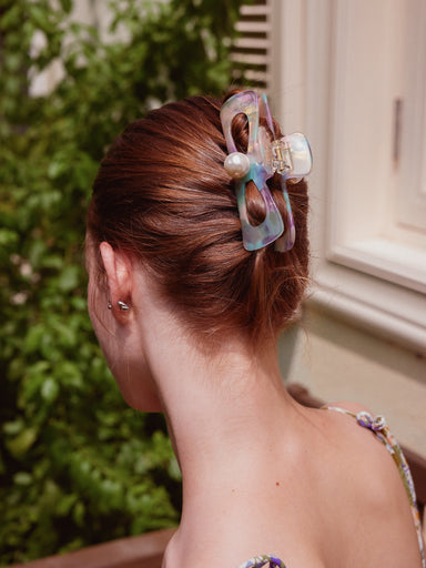 A woman shown from the back wearing a translucent iridescent cellulose acetate hair claw clip with a pearl accent, holding her auburn hair in a low bun.