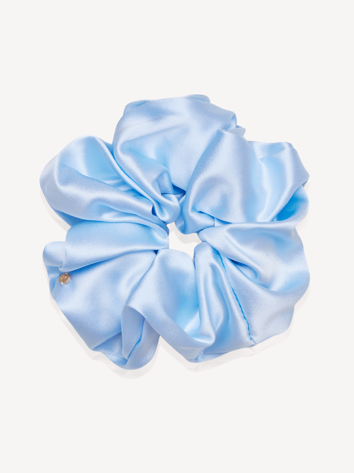 A light blue silk hair scrunchie with a small gold logo plate detail, shown on a clean off-white background.
