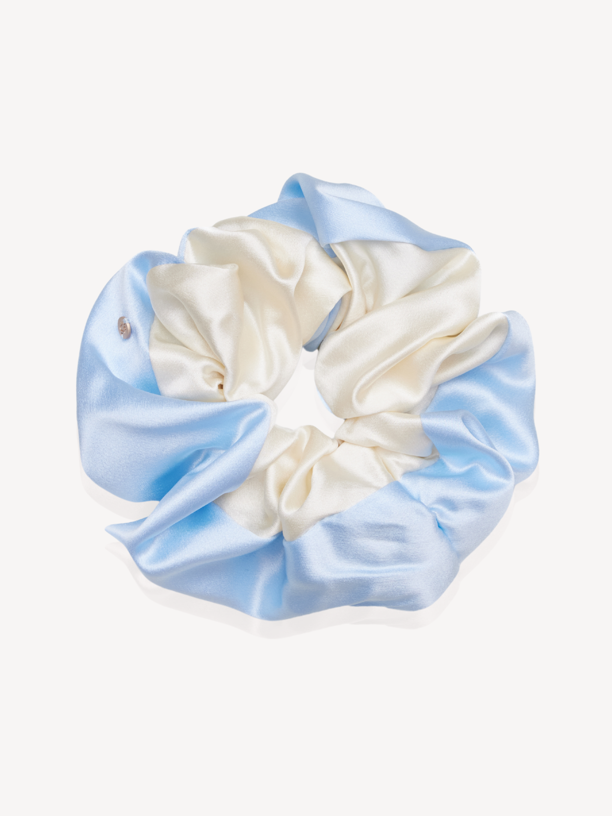 A silk hair scrunchie featuring a color-blocked design of light blue and cream, with a small silver rhinestone accent on the left side, set against a plain off-white background.