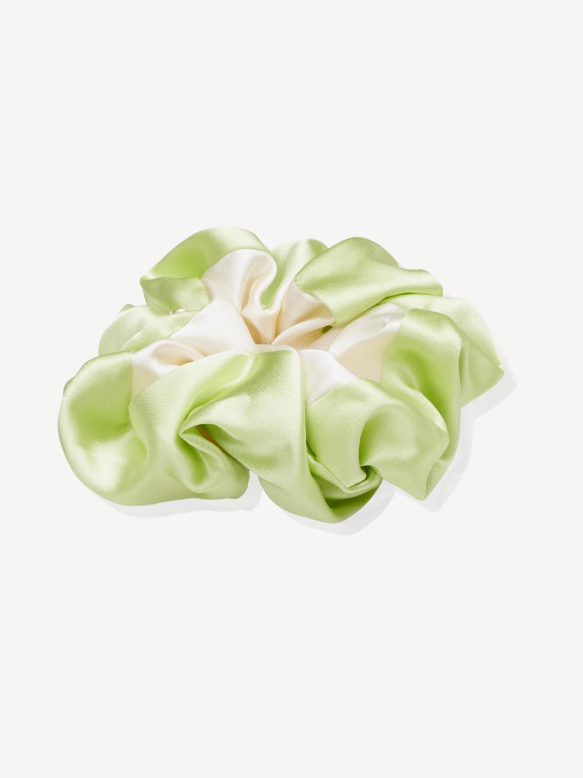 A silk hair scrunchie in a light pastel green and cream color combination, displayed on a clean off-white background.