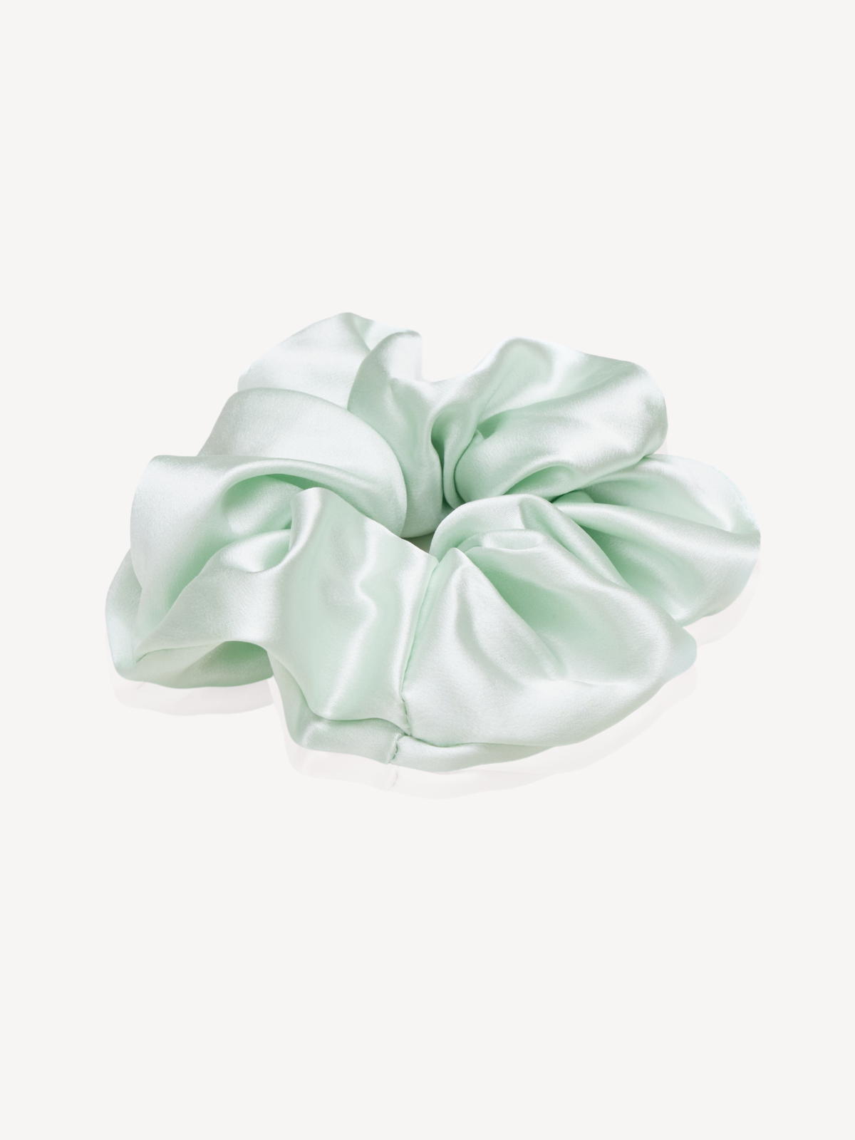 A mint green silk hair scrunchie on a clean, off-white background.