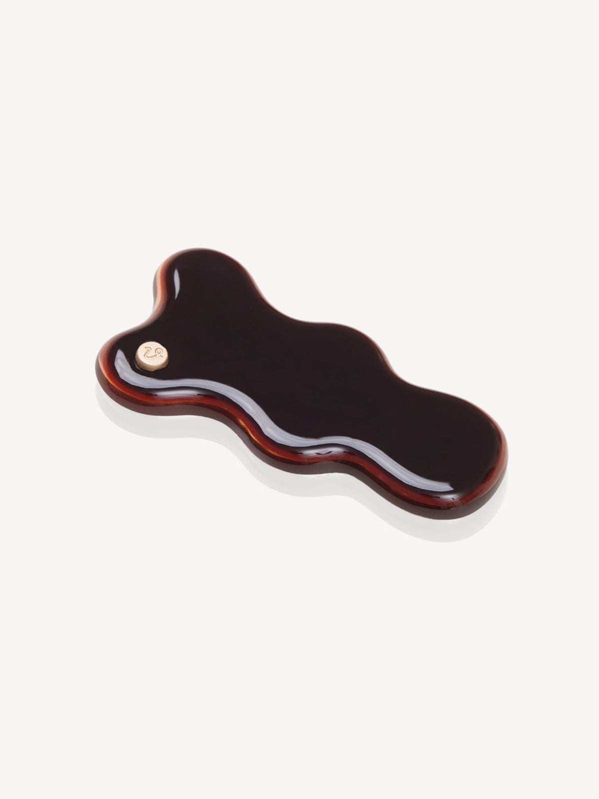 A glossy, wavy-shaped cellulose acetate hair claw clip in a dark brown color with a small gold-tone metal rivet, shown on a light gray background.
