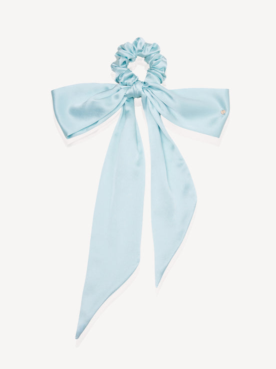 A light blue silk scrunchie with a matching long bow, displayed on a clean off-white background.