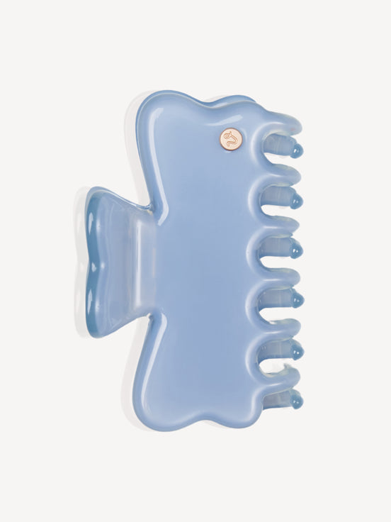 A light blue translucent cellulose acetate hair claw clip with a small gold-tone decorative button on the back, shown against a plain off-white background.