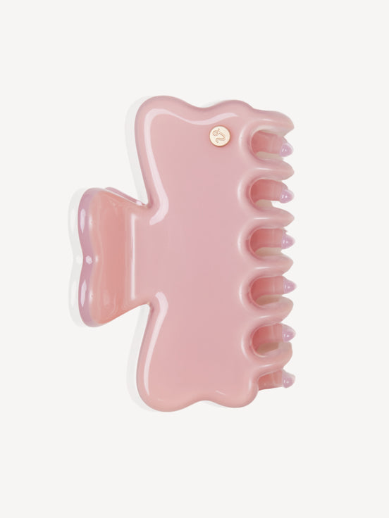 A glossy light pink cellulose acetate hair claw clip with a small gold brand emblem, shown on a clean off-white background.
